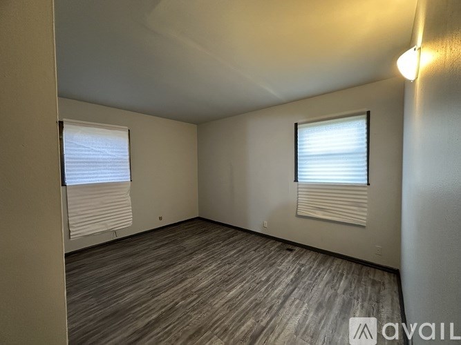 A room with wooden flooring and two windows with blinds.