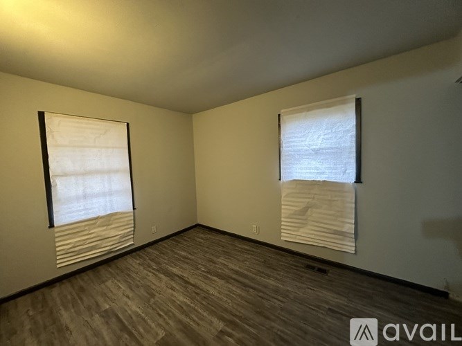 A room with wooden flooring and two windows covered with white blinds.