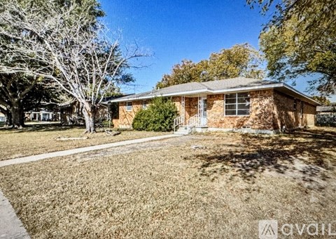 A house with a brown brick exterior and a white door is surrounded by trees and grass.