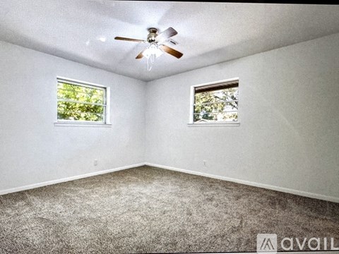 A room with a carpeted floor, a ceiling fan, and two windows.