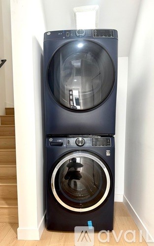 A front-loading washing machine with a transparent door is placed in a room.