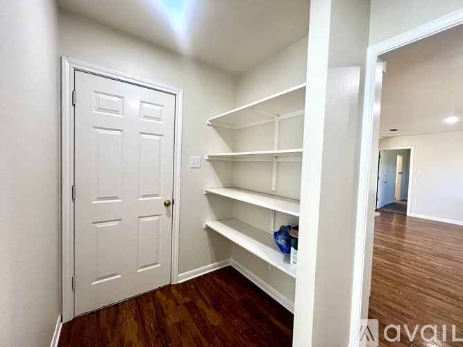 A white door is on the left of a room with a white wall and a white shelving unit.