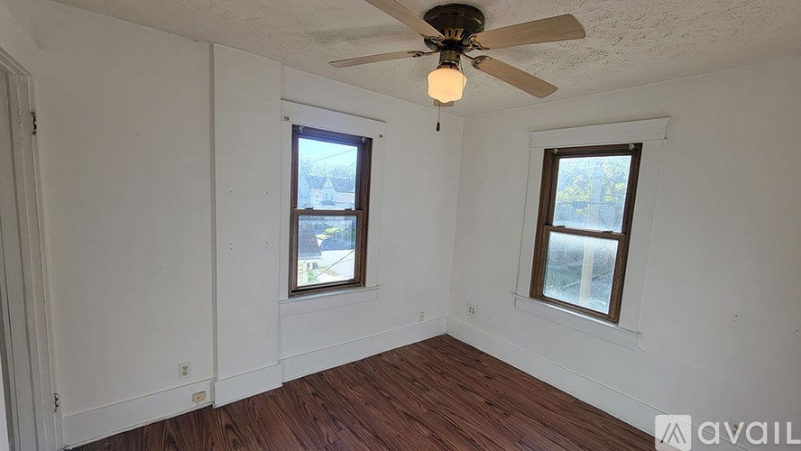 A room with a ceiling fan and two windows.
