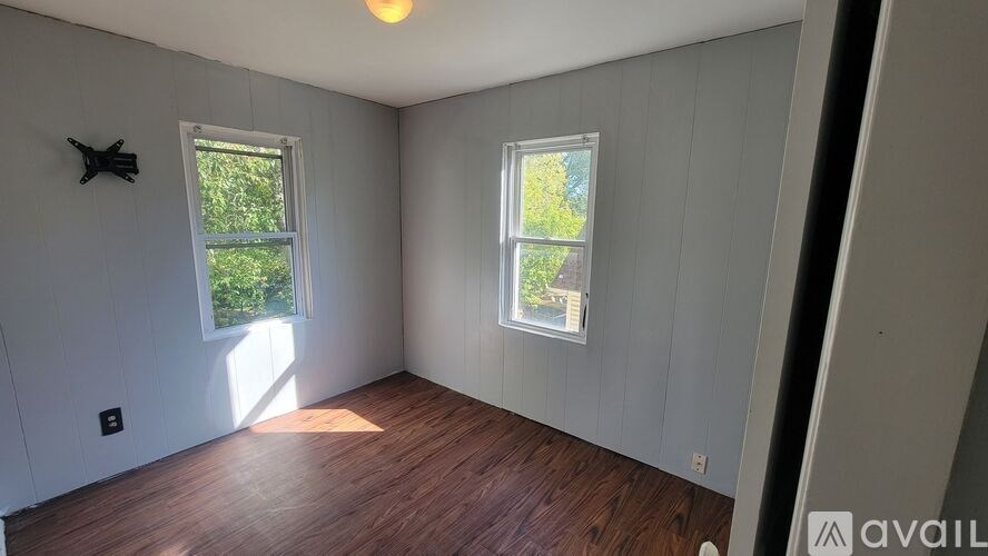 A room with wooden floors and two windows showing greenery outside.
