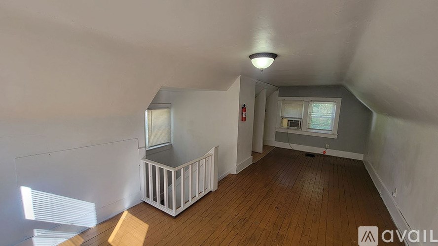A room with wooden floors and white walls, with a window and a fire extinguisher visible.
