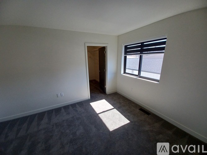A room with a carpeted floor, a window with blinds, and a door leading to another room.