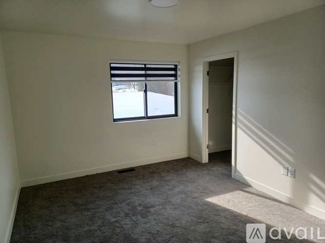 A room with a carpeted floor, a window with blinds, and a door leading to another room.