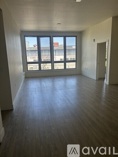 A large empty room with wooden floors and a view of the Ford Street Studio building outside the window.