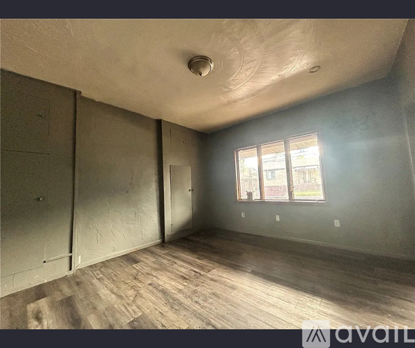 A room with wooden flooring and a window with a view of trees.