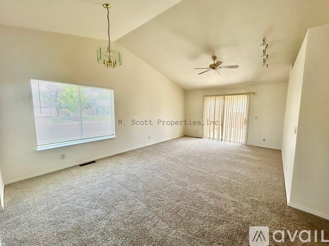 A spacious room with a carpeted floor, a ceiling fan, and a window with blinds.