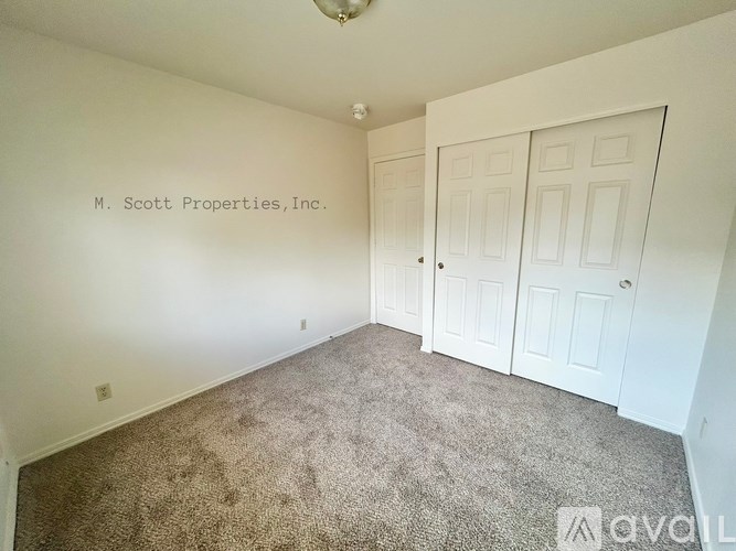 A room with carpeted floor and white walls with a ceiling fan.