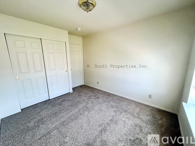A room with carpeted floor and two doors, with a logo for M. Scott Properties, Inc. on the wall.