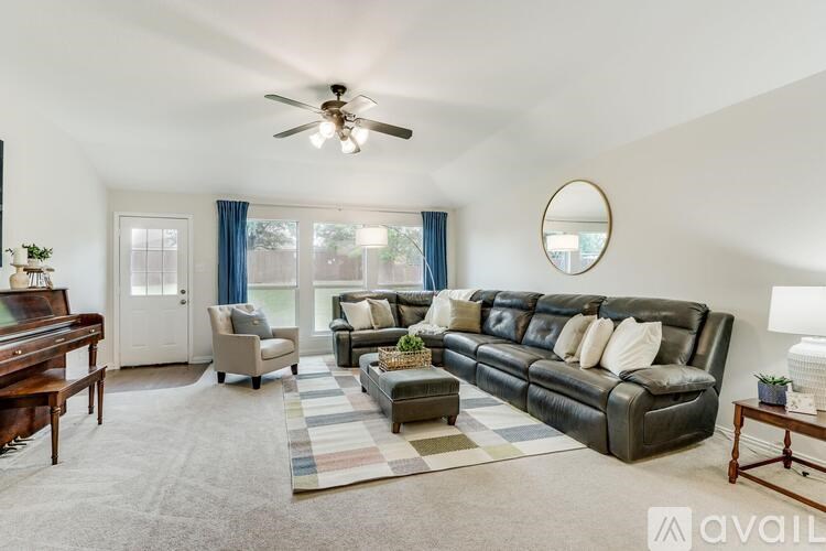 A living room with a black leather couch, a wooden piano, a rug, and a ceiling fan.