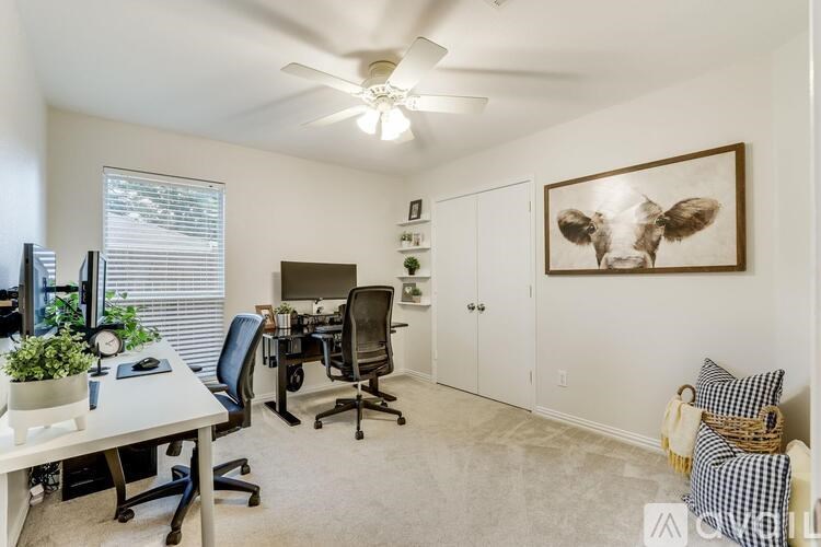 A room with a ceiling fan and a painting of a cow on the wall.