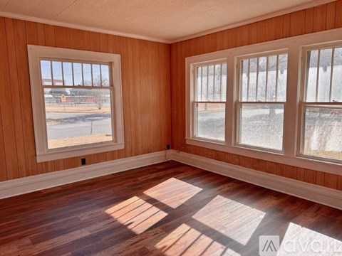 A room with wooden walls and floors has two windows.