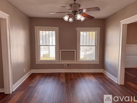 A room with a ceiling fan and two windows.