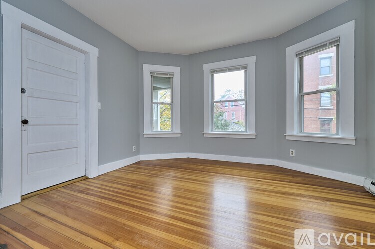 A room with a white door, two windows, and wooden flooring.
