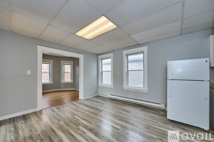 A spacious room with a white refrigerator and wooden flooring.