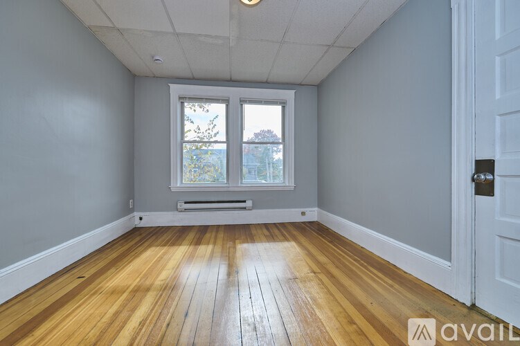 A room with wooden floors and a window with a view of trees and a building outside.