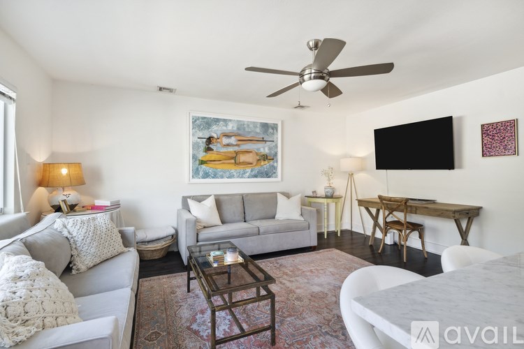 A living room with a grey couch, a coffee table, a ceiling fan, and a painting on the wall.