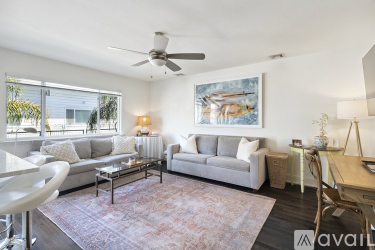 A living room with a grey couch, a rug, a painting, and a ceiling fan.