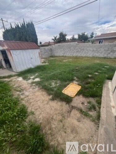 A backyard with a fence, shed, and a small patch of dirt.