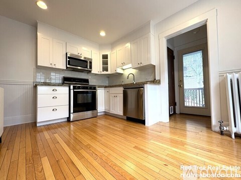 A kitchen with white cabinets and wooden floors.