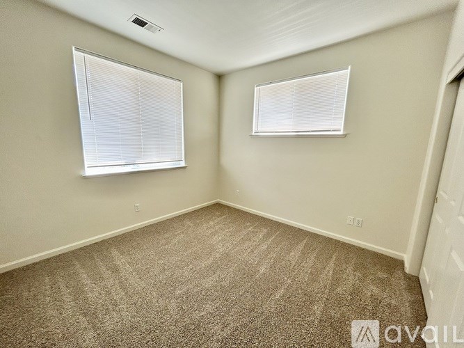 A room with carpeted floor and two windows with blinds.