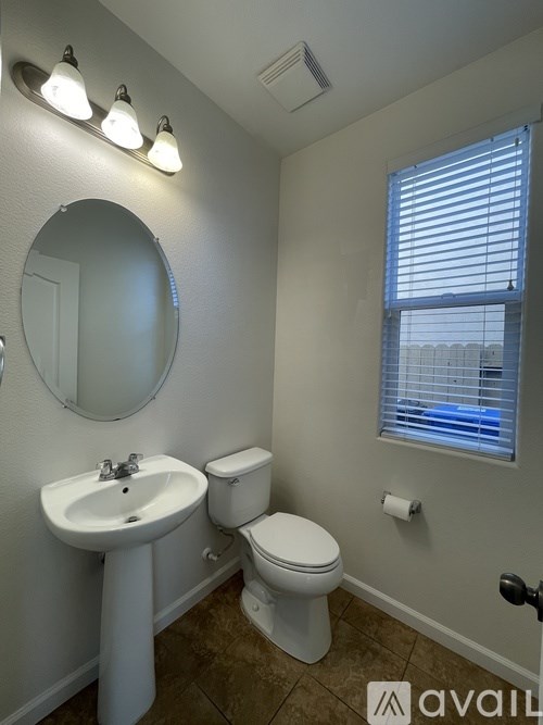 A bathroom with a toilet, sink, mirror, and window.