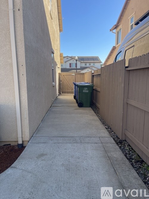 A narrow sidewalk between two houses with a green dumpster in the distance.