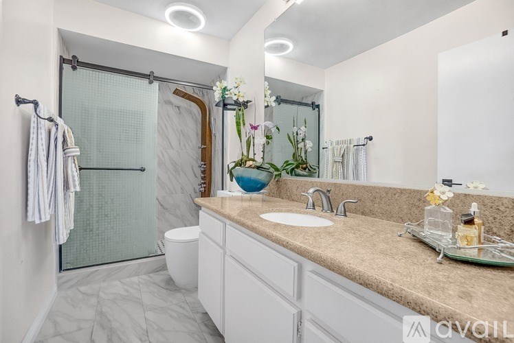 A bathroom with a glass shower door and a marble countertop.