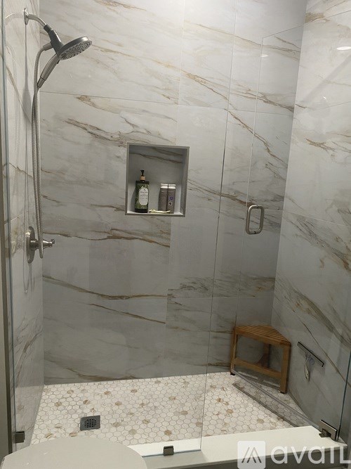 A marble tiled shower with a glass door and a small wooden stool.