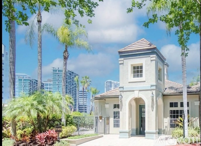 A small building with a tower is surrounded by trees and plants.