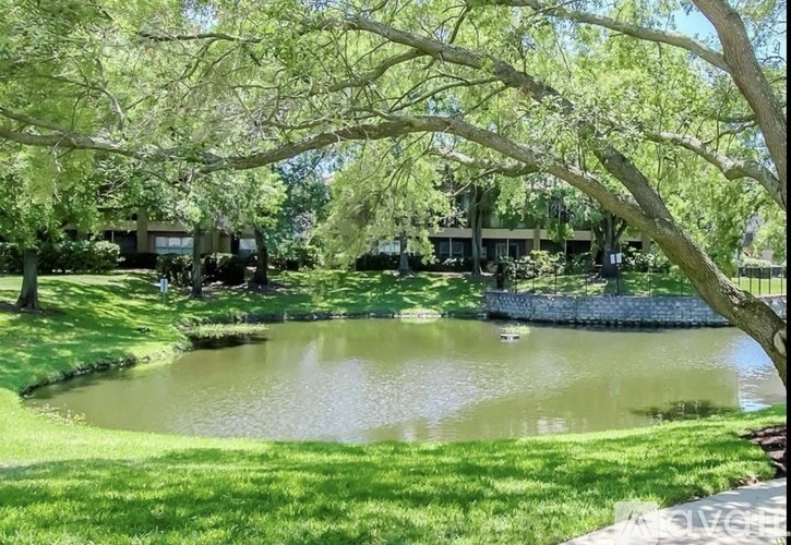 A serene landscape with a pond, trees, and buildings in the distance.