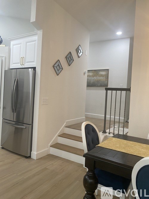 A kitchen with a refrigerator, stairs, and a dining table.