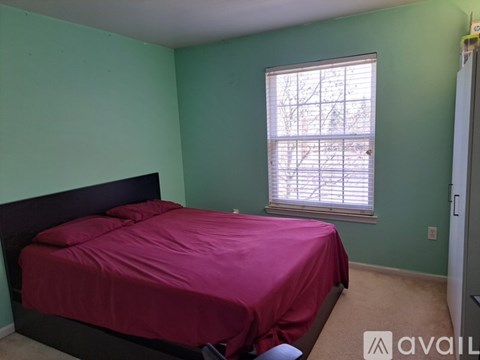 A bedroom with a bed covered in a pink sheet and a window with blinds.