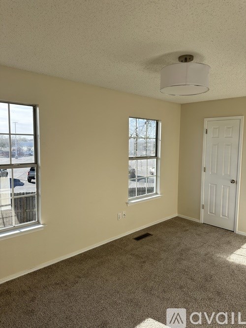 A room with a carpeted floor, a ceiling light, and a door.
