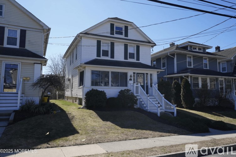A white house with a black roof and a grey house in the background.