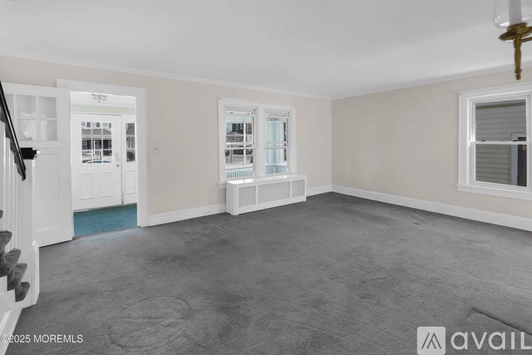 A room with a carpeted floor and a staircase on the left side.