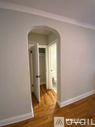 A hallway with a wooden floor and white walls leading to a bathroom.