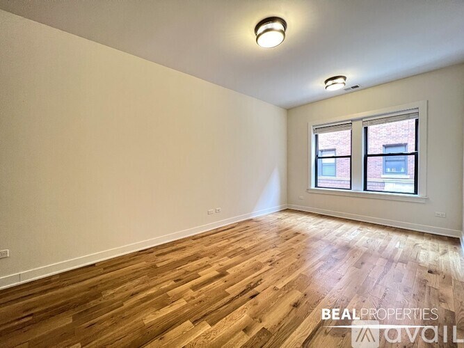 A room with wooden flooring and a window showing a brick building outside.