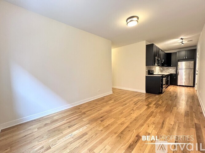 A room with wooden flooring and a kitchen area in the background.