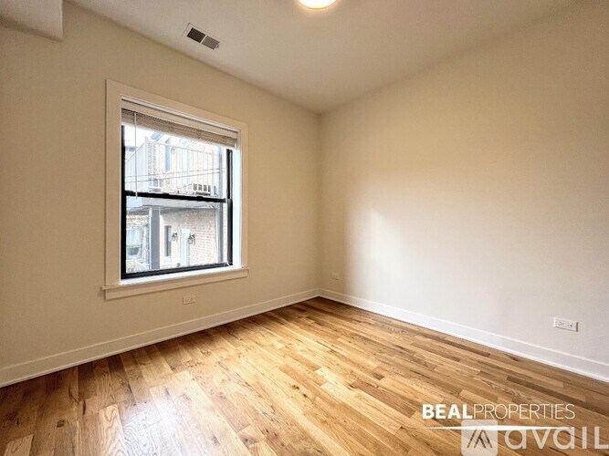 A room with wooden flooring and a window showing a view of a building outside.