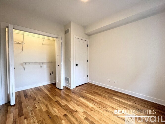 A room with wooden flooring and white walls, with a doorway leading to another room.