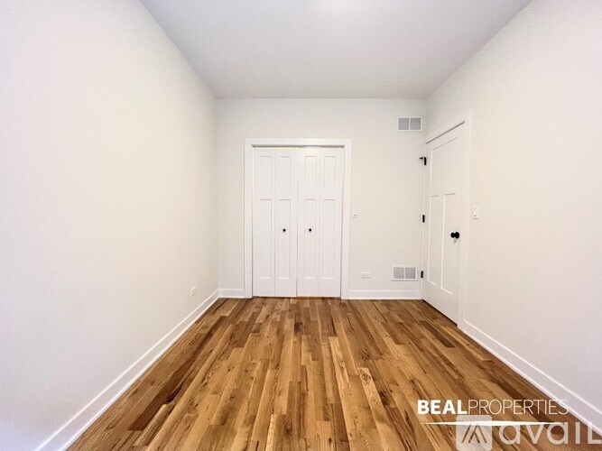 A room with wooden flooring and white walls, with a door and a small window.