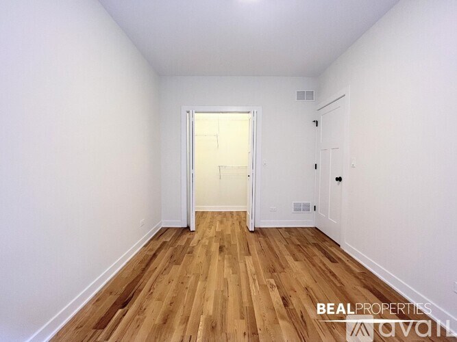A room with wooden flooring and white walls, with a doorway leading to another room.