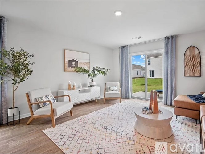 A living room with a white sofa, a wooden armchair, and a large window with a view of the outdoors.