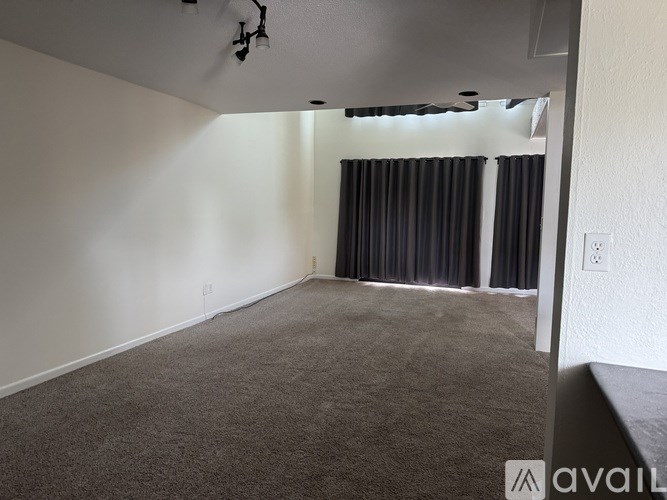A room with carpeted floor and a window with curtains.
