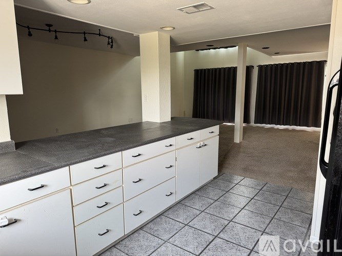 A room with white cabinets and drawers, a grey countertop, and a tiled floor.