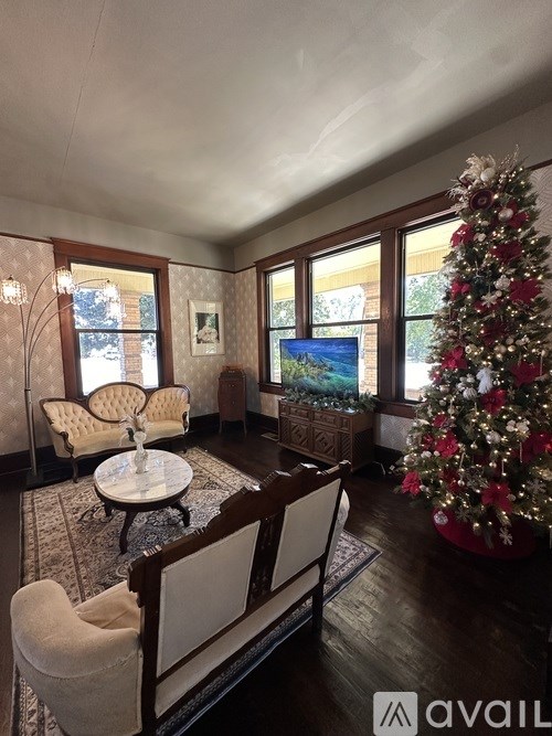 A Christmas tree stands in a living room with a couch and chairs.